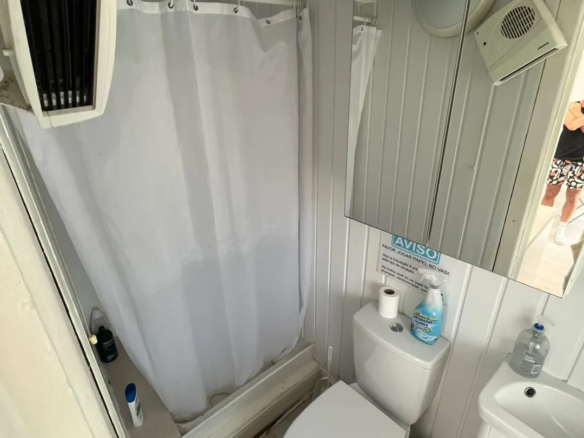 Small bathroom with toilet, shower curtain, sink, and warning sign.