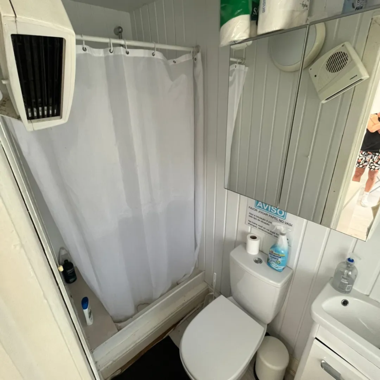 Small bathroom with toilet, shower curtain, sink, and warning sign.