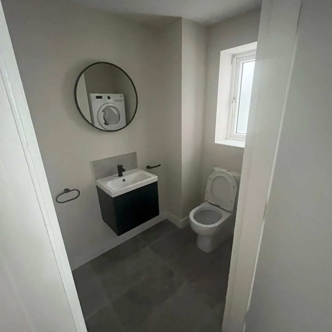 Small bathroom with toilet, sink, mirror, and gray tile floor.