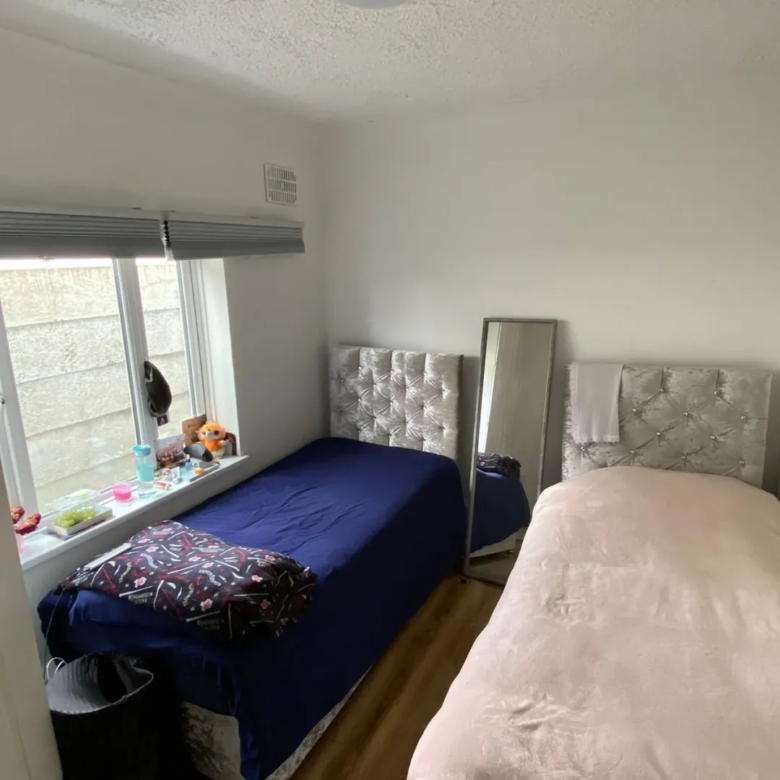 Small bedroom with two single beds, window, mirror, and wood floor.