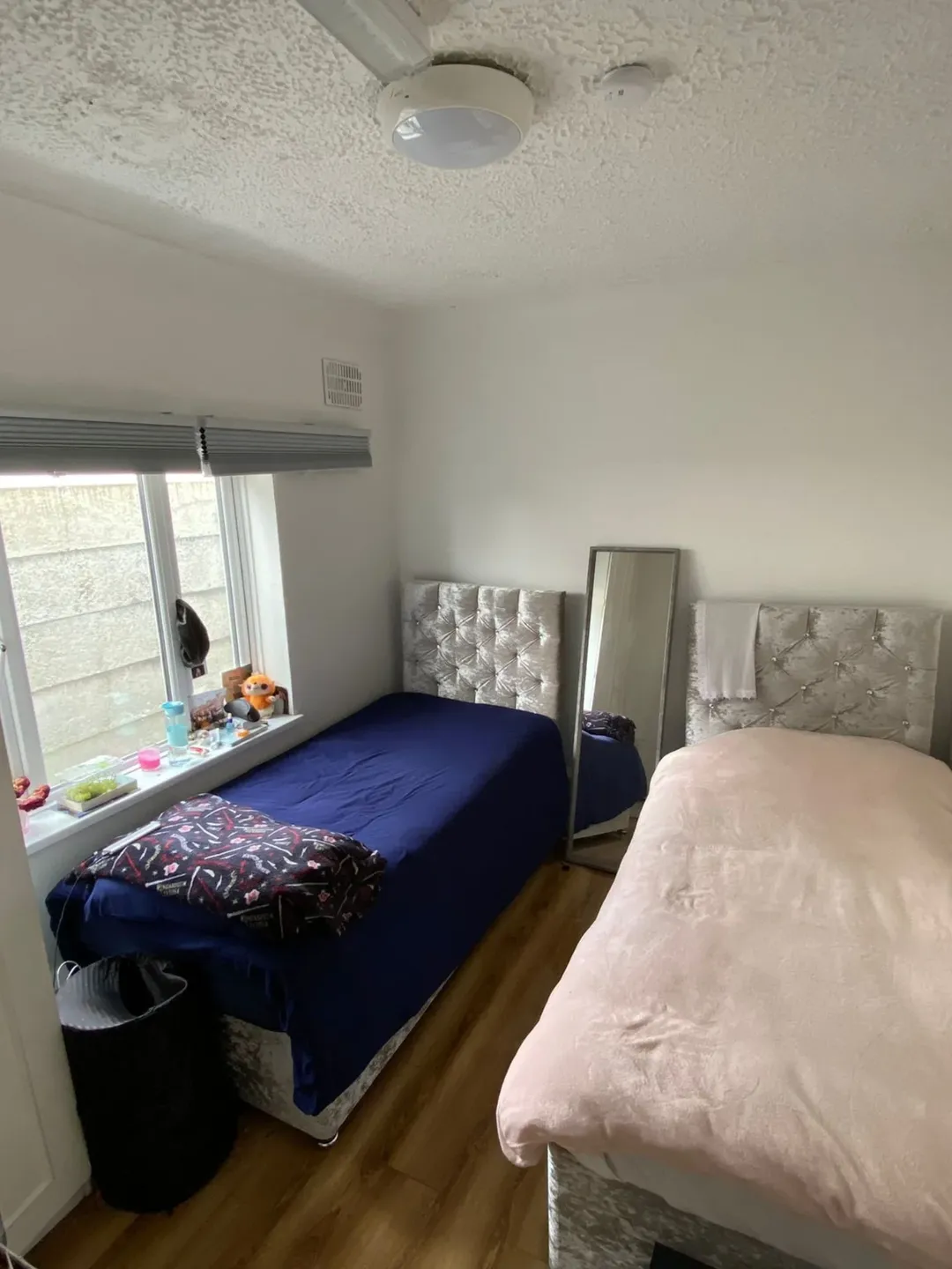 Small bedroom with two single beds, window, mirror, and wood floor.