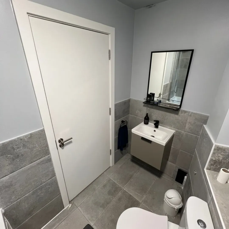 Small gray bathroom with toilet, sink, mirror, and gray tile walls.