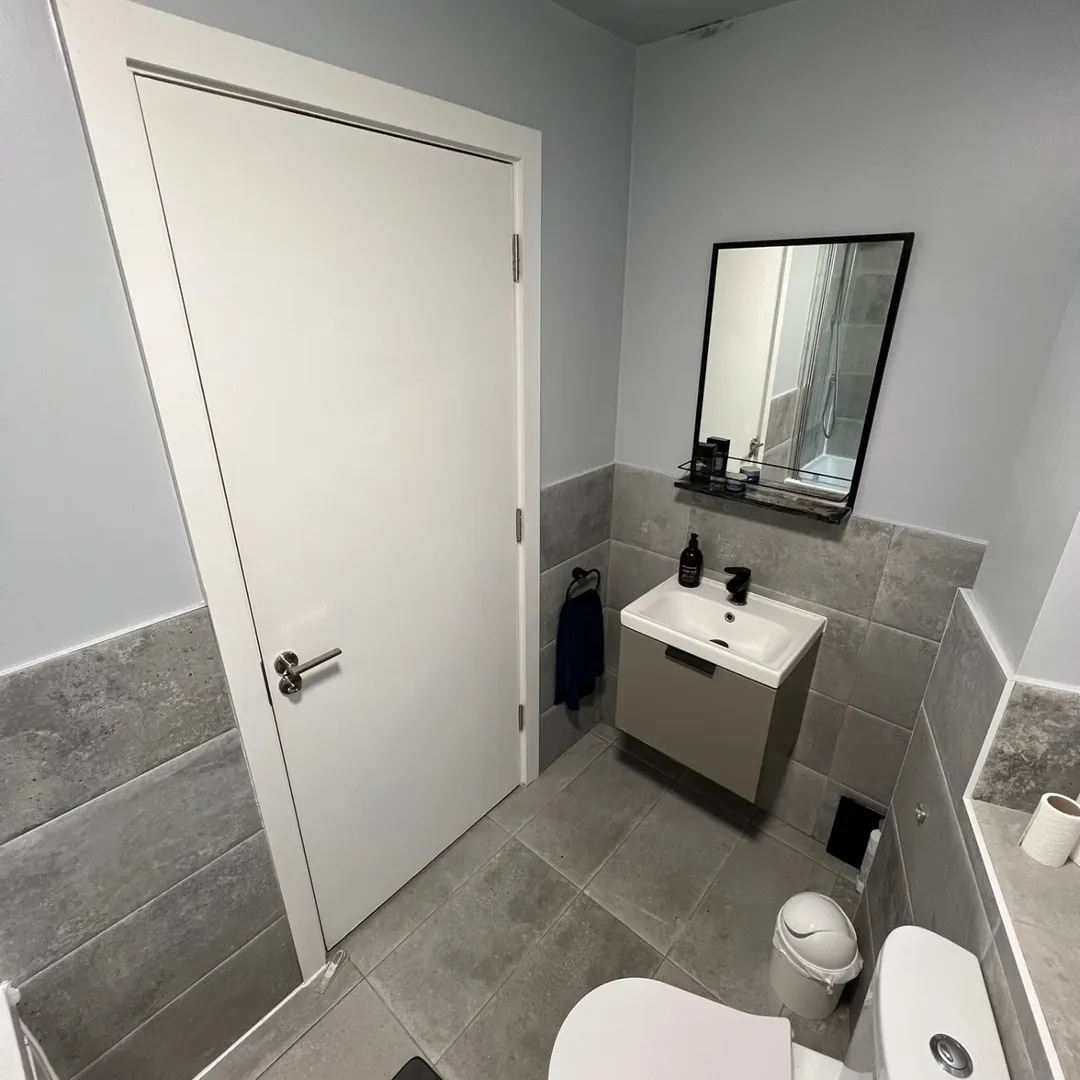 Small gray bathroom with toilet, sink, mirror, and gray tile walls.