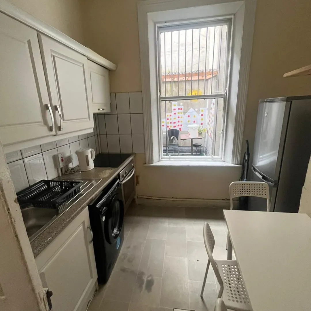 Small Kitchen White Cabinets Appliances 1 Small kitchen with white cabinets, appliances, table, and a window overlooking a courtyard.