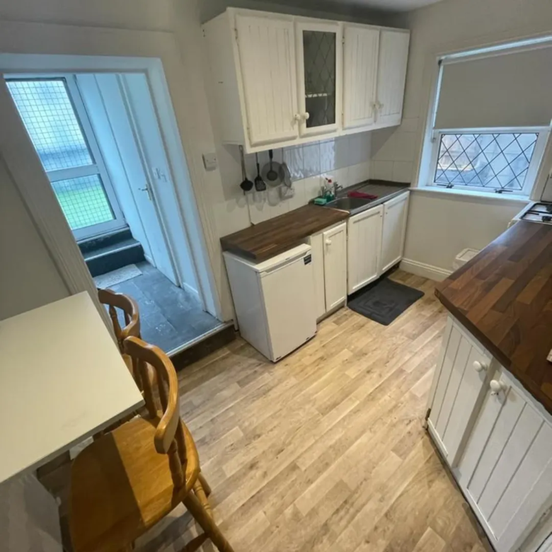 Small kitchen with white cabinets, wooden countertops, and dining area near the entrance.