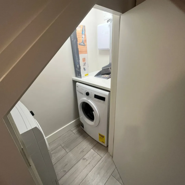 Compact laundry space with stacked washer dryer, cleaning supplies, gray tile.