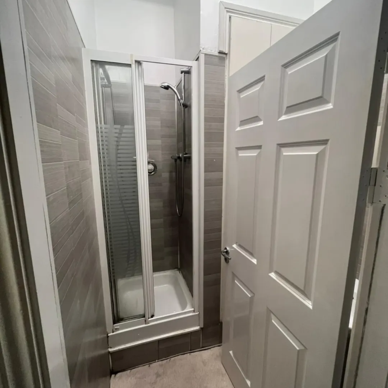 Small shower stall in bathroom with grey tile and white door.