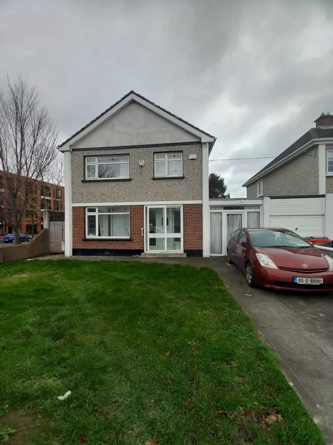 Two-story house with brick and gray stucco exterior, green lawn, and red car parked in driveway on overcast day.