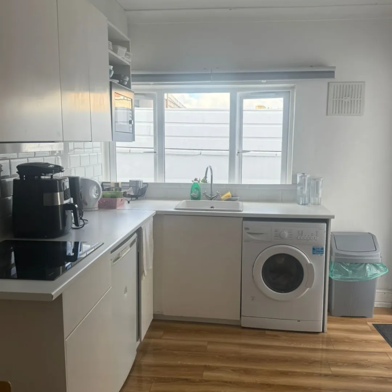 Bright white kitchen with washing machine, sink, and window.
