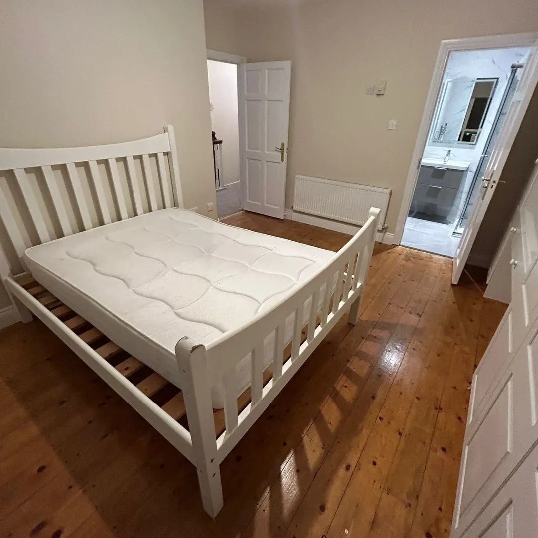 White Wooden Bed Frame Bedroom White wooden bed frame with mattress in bedroom, bathroom doorway visible.