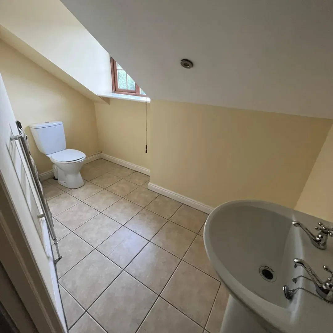 Attic Bathroom Toilet Sink Tiled Floor Attic bathroom with toilet, sink, tiled floor, and angled ceiling under a window. Neutral color scheme.