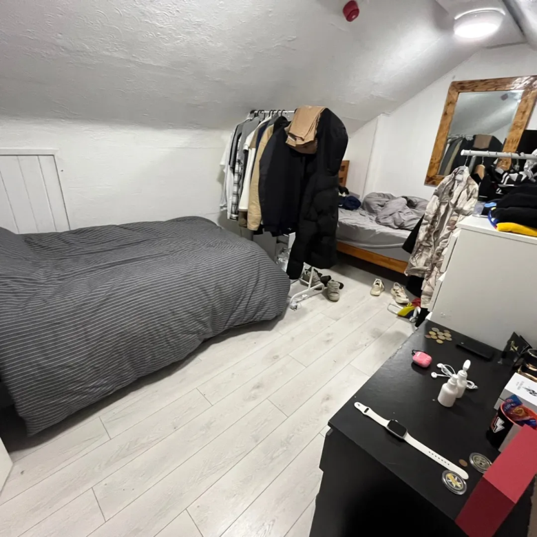 Cozy attic bedroom with bed, clothes rack, and desk. Natural light.