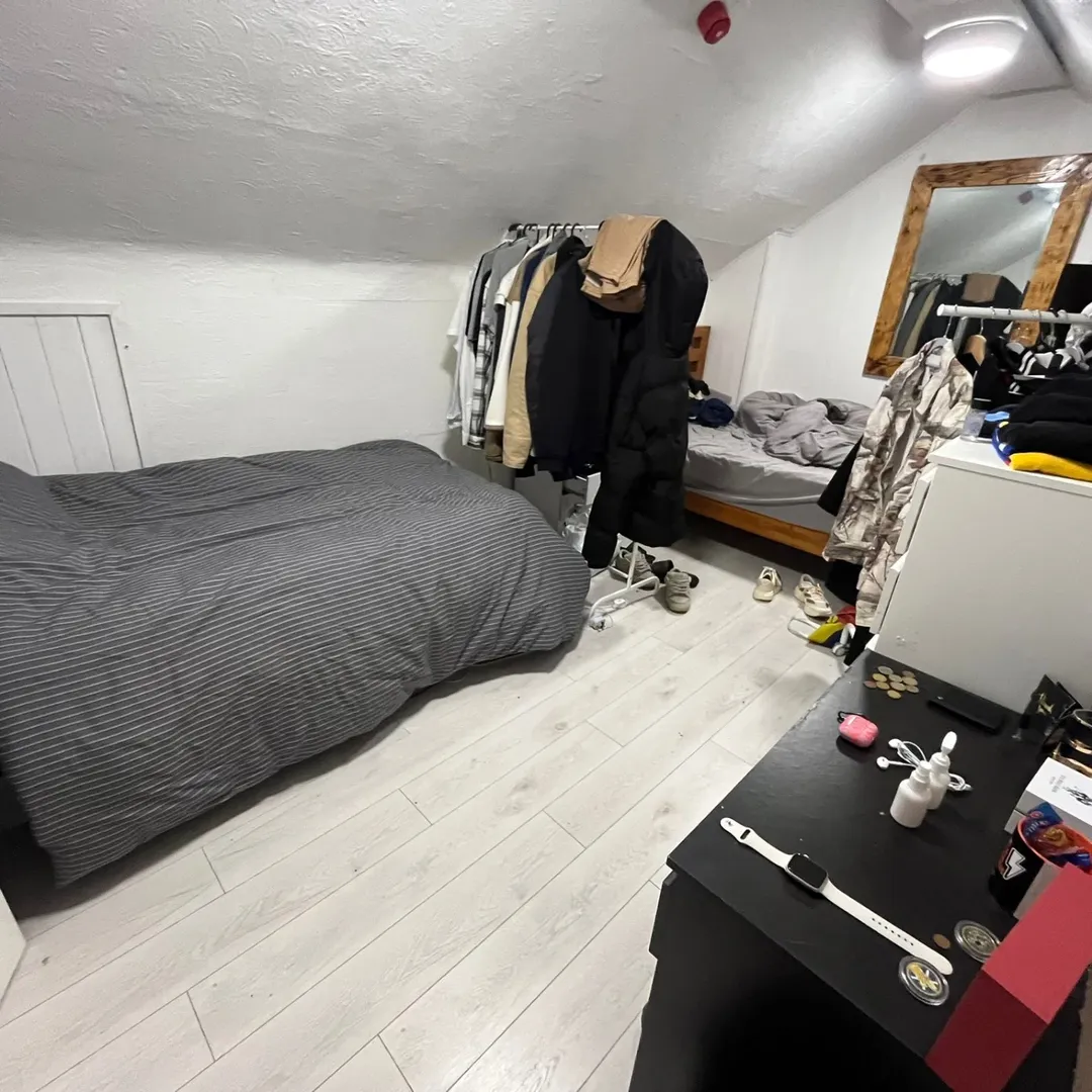 Cozy attic bedroom with bed, clothes rack, and desk. Natural light.