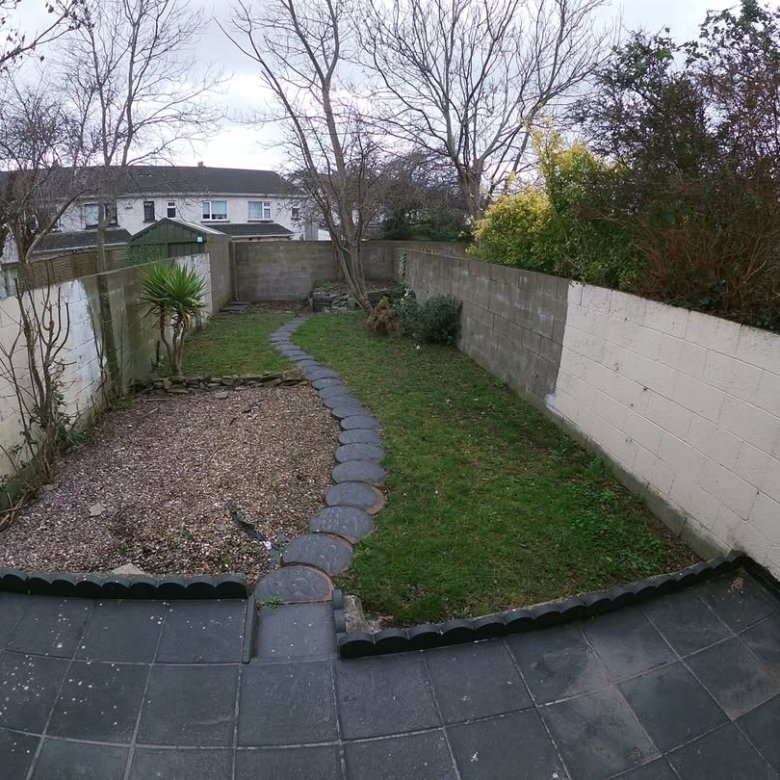 Backyard with stone path, grass, gravel, and concrete walls on a cloudy day.