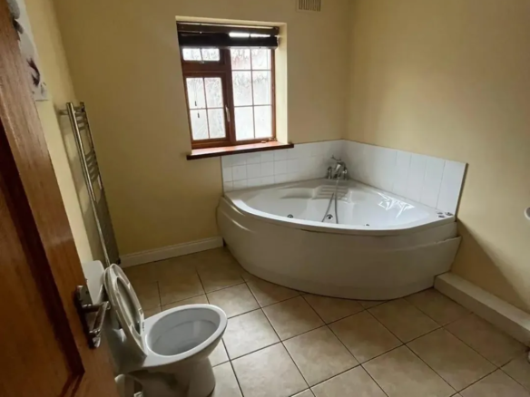 Bathroom with corner jacuzzi tub, toilet, heated towel rack, and window.