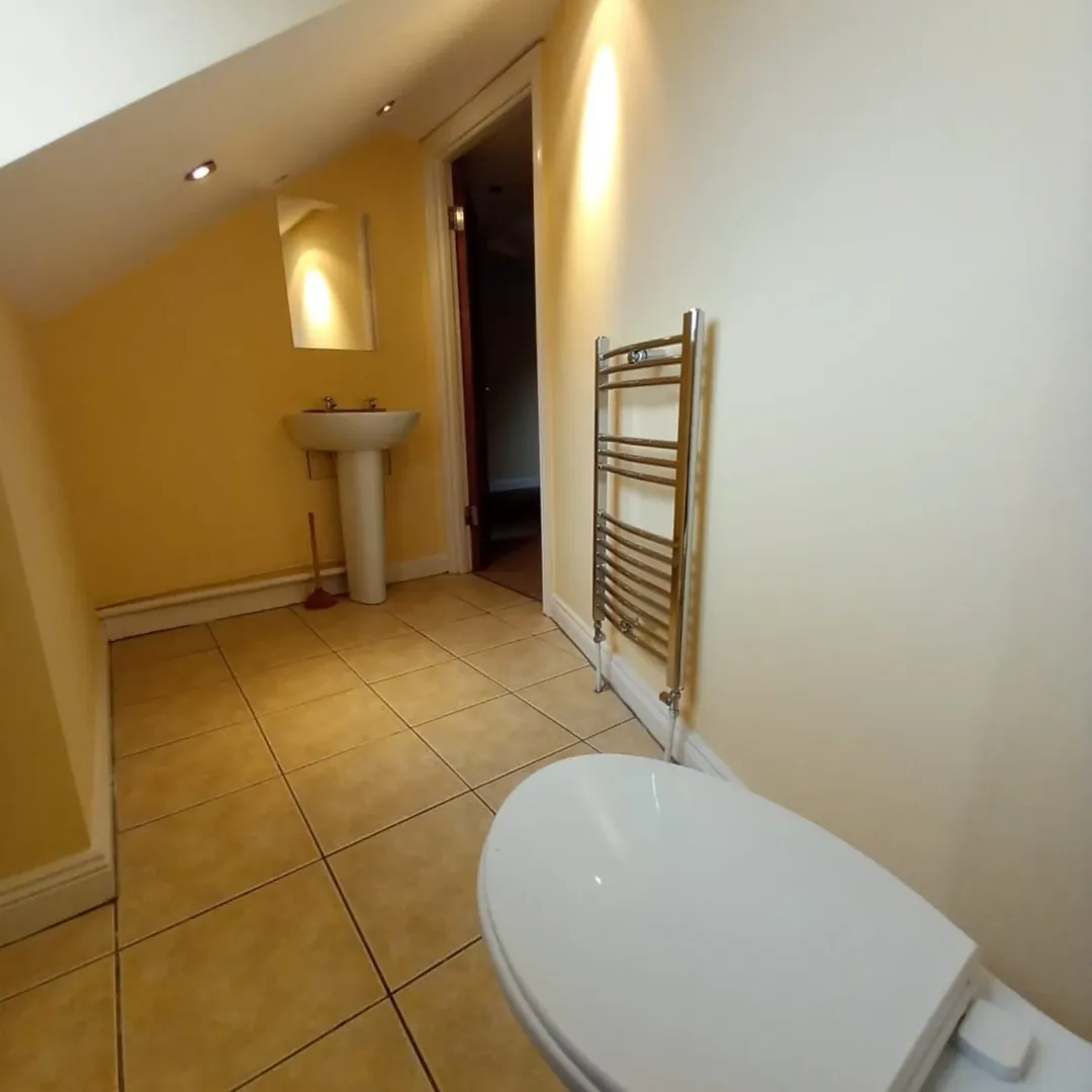 Bathroom Toilet Sink Towel Warmer Bathroom with toilet, sink, towel warmer, and yellow walls under sloped ceiling.
