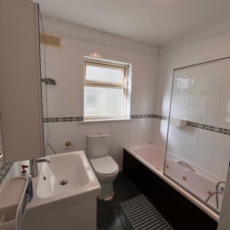 Bathroom with white tiles, dark wood bath panel, and window above toilet.