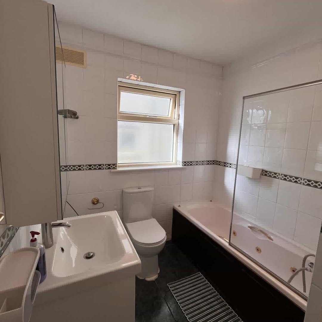 Bathroom with white tiles, dark wood bath panel, and window above toilet.