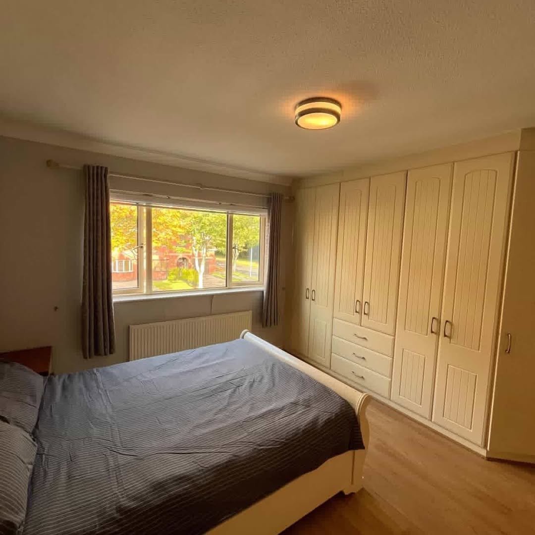 Bedroom with bed, built-in wardrobe, window, and warm lighting. Neutral color scheme.
