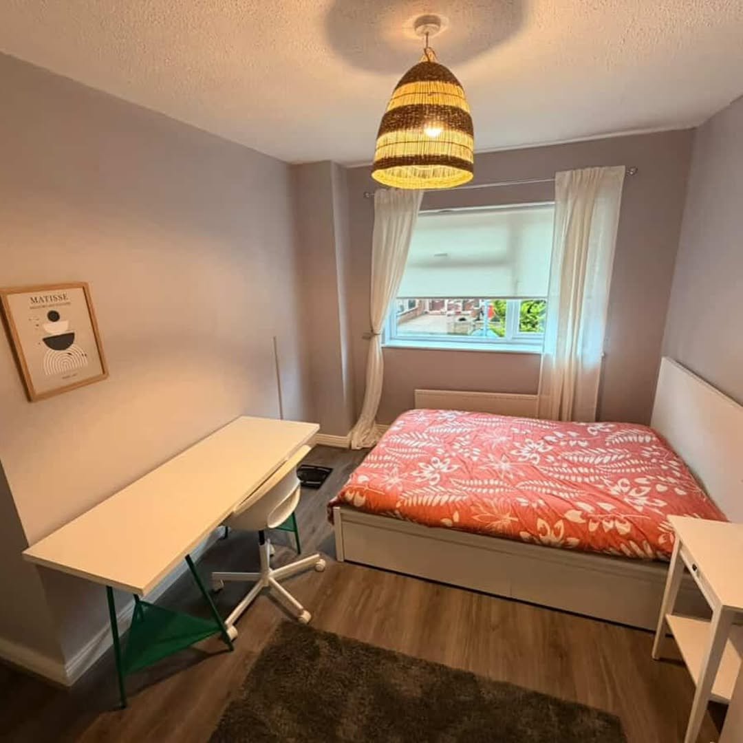 Cozy bedroom with bed, desk, rug, and Matisse art print. Woven pendant light fixture.