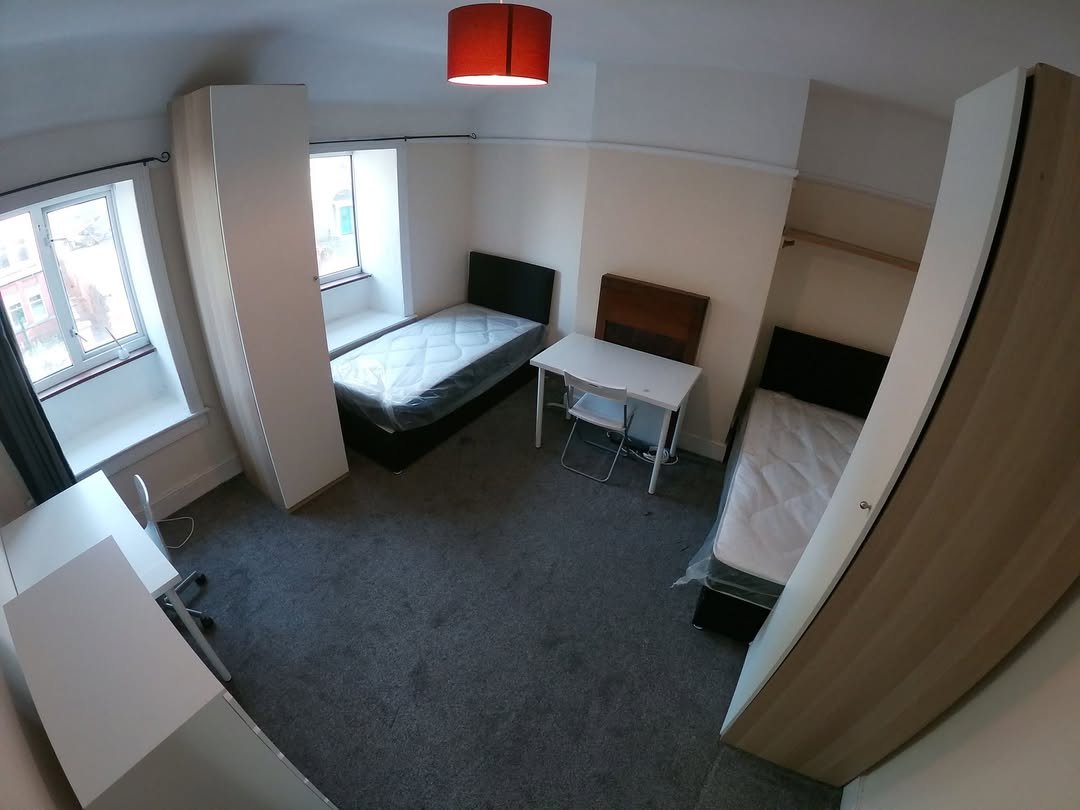 Bedroom with two single beds, desks, wardrobes, and a red lampshade. Window provides natural light.