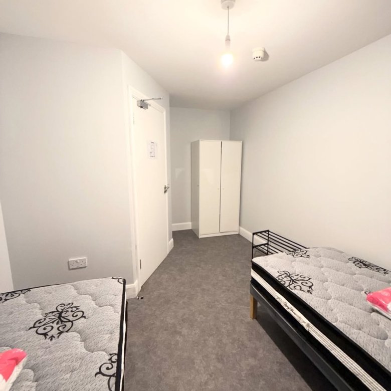 Bedroom with two single beds, wardrobe, and white door. Minimalist interior design with gray carpet.