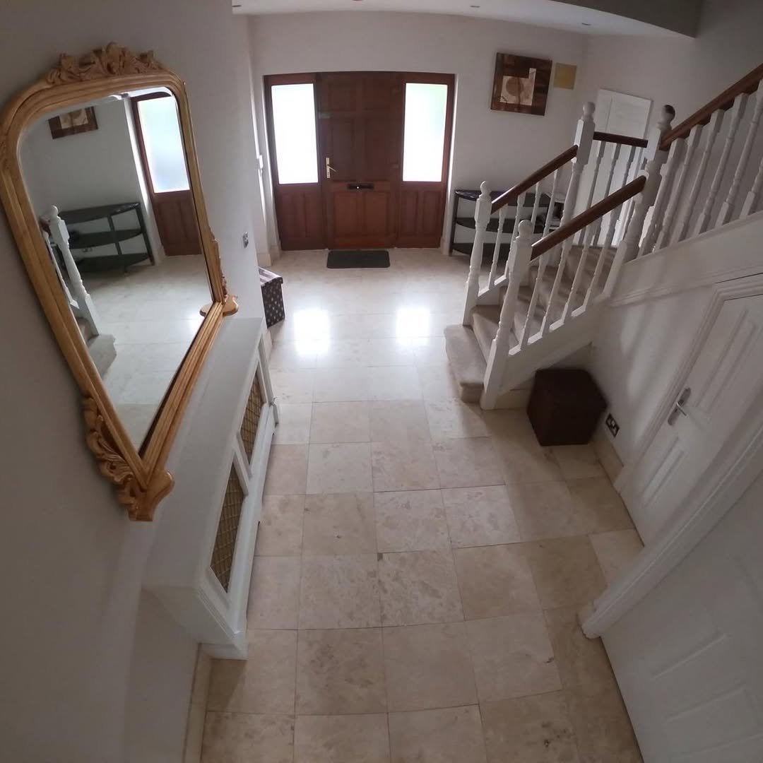 Bright Hallway Travertine Tile Gold Mirror Bright hallway with travertine tile, wooden front door, staircase, gold mirror, and white radiator cover.
