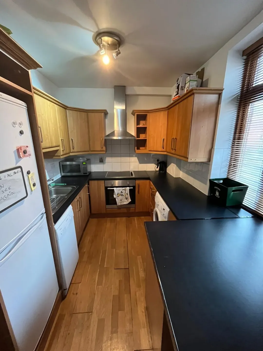 Compact Kitchen Wood Cabinets Black Countertops Compact kitchen with wood cabinets, black countertops, and white appliances.