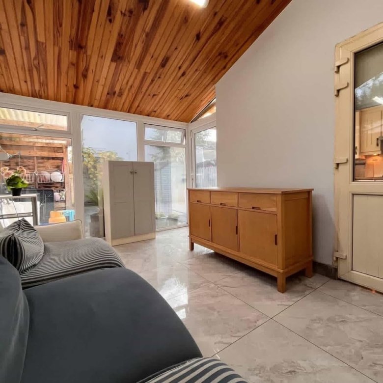 Conservatory interior with wooden ceiling, cabinet, and gray sofa. Bright, airy space.