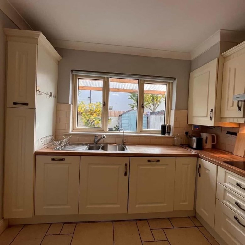 Cream kitchen with sink under window, wooden countertops and tile backsplash.