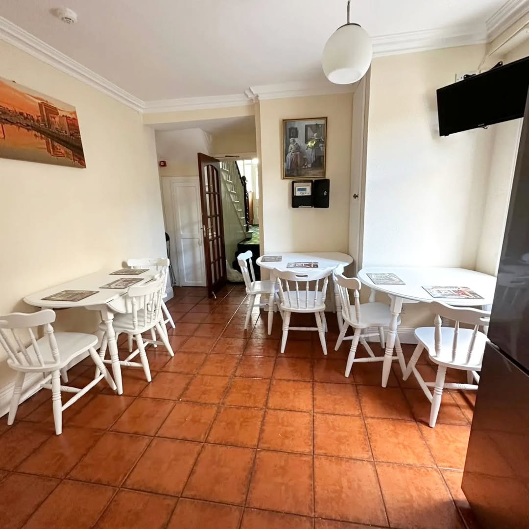 Cozy dining area with white tables and chairs, terracotta tile floor, and artwork on the walls.