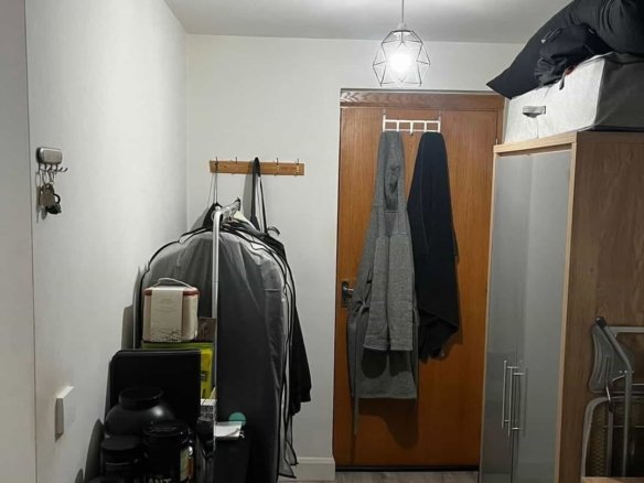 Hallway with storage cabinet, coats hanging on door, and black rug.