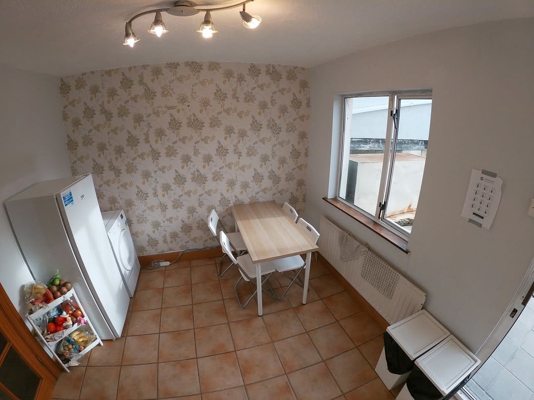 Kitchen dining area with table, chairs, washing machine, refrigerator, patterned wallpaper, and tile floor.