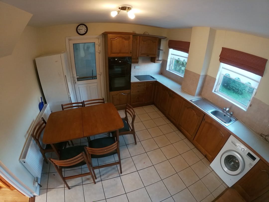 Cozy kitchen with wooden cabinets, dining table, and white appliances. Clock on wall.