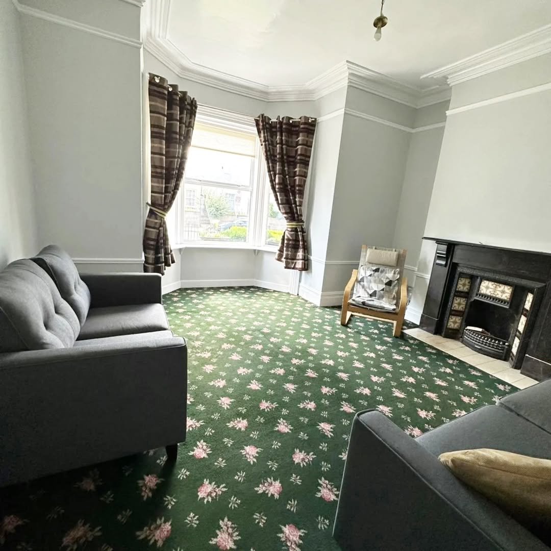 Living room with green floral carpet, gray sofa, bay window, and fireplace.