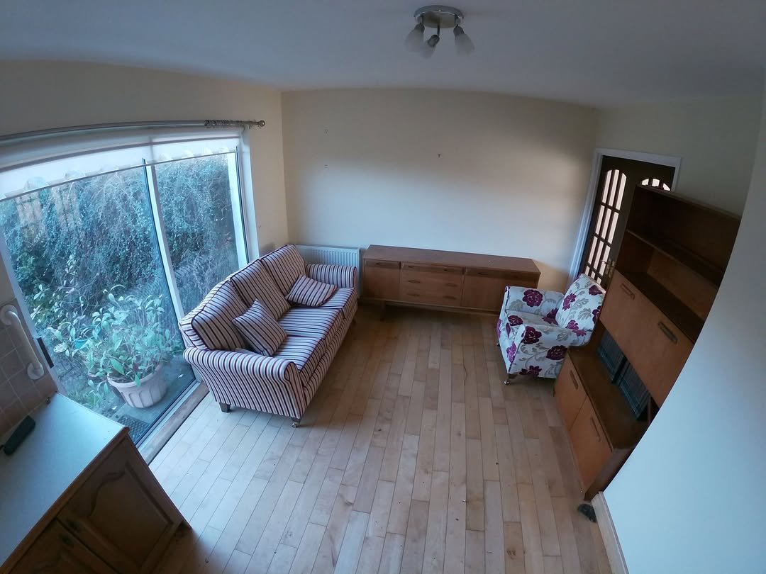 Living room with striped sofa, floral armchair, and wooden furniture. Garden view through large window.