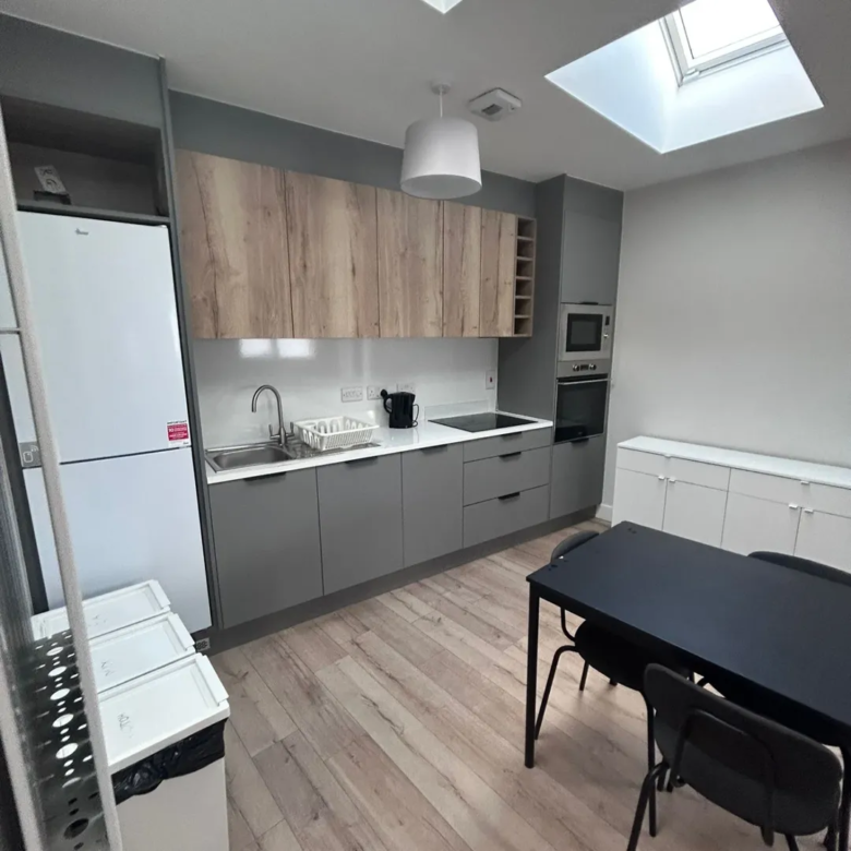 Modern kitchen with gray cabinets, wood accents, skylights, and a black dining table.