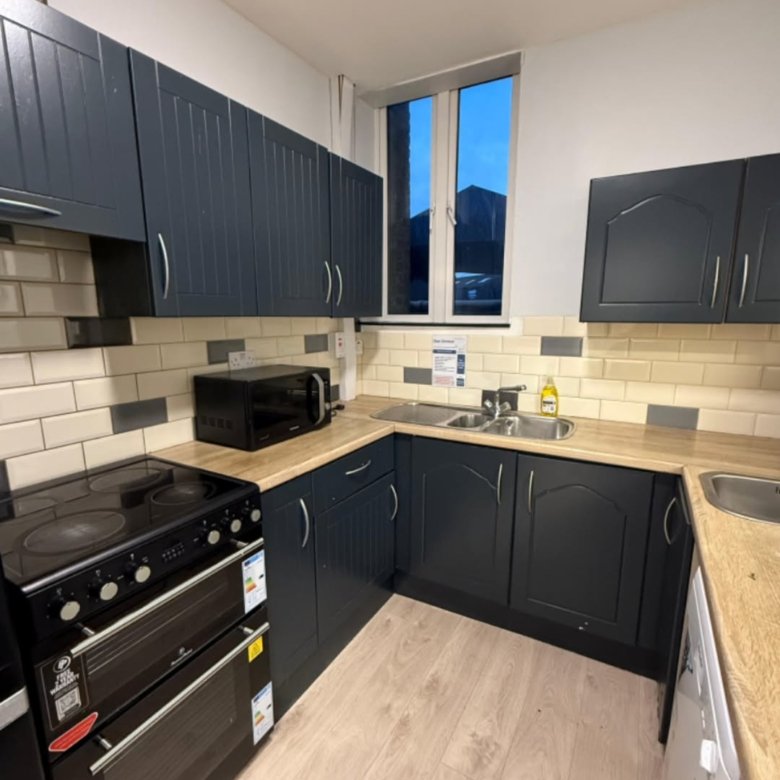 Modern kitchen with dark blue cabinets, oven, microwave, and sink.