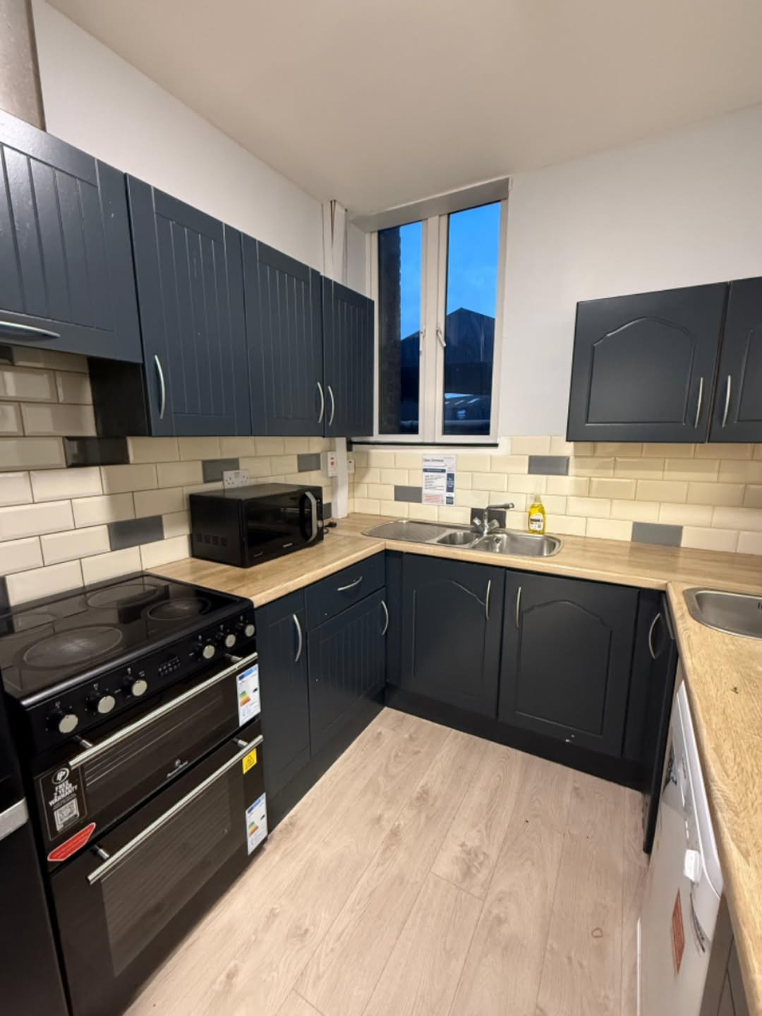 Modern kitchen with dark blue cabinets, oven, microwave, and sink.