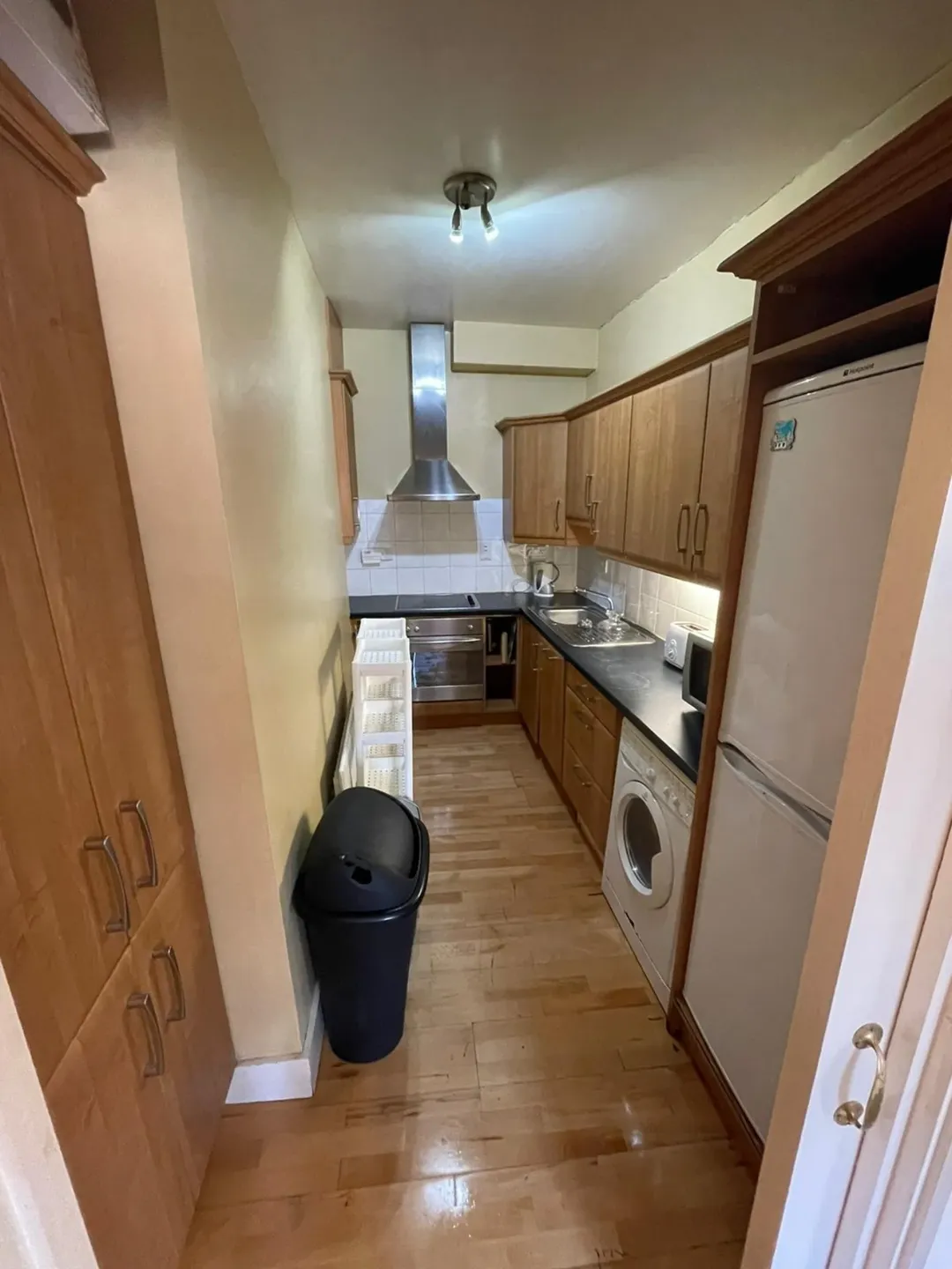 Narrow kitchen with wooden cabinets, stainless steel appliances, and a washing machine.