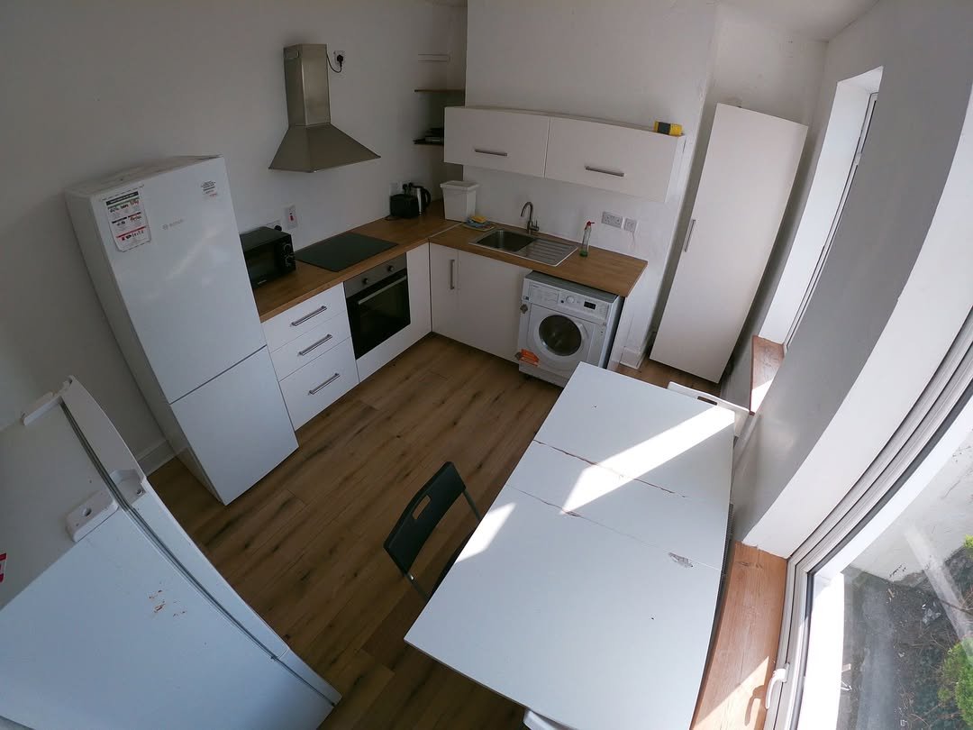 Compact kitchen with white cabinets, appliances, table, and chair in a small apartment.
