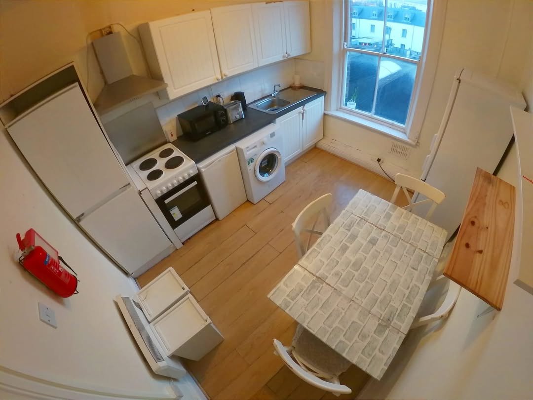 Small Apartment Kitchen White Appliances Table Compact kitchen with white cabinets, appliances, dining table, and chairs in a small apartment setting.