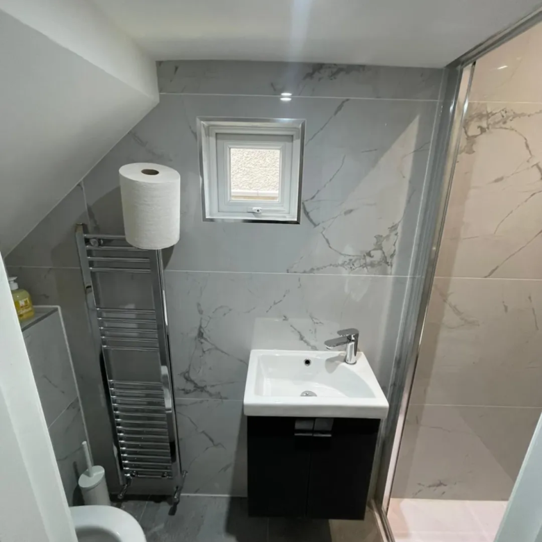 Small bathroom with gray marble tiles, sink, towel warmer, and toilet.