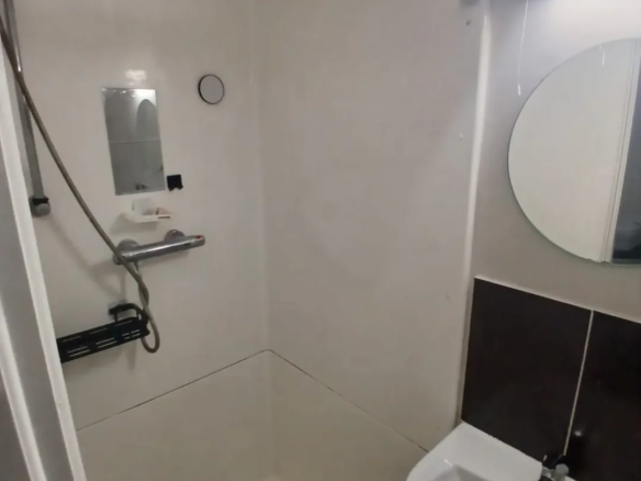 Small bathroom interior with shower, sink, mirror, and brown tile accent.