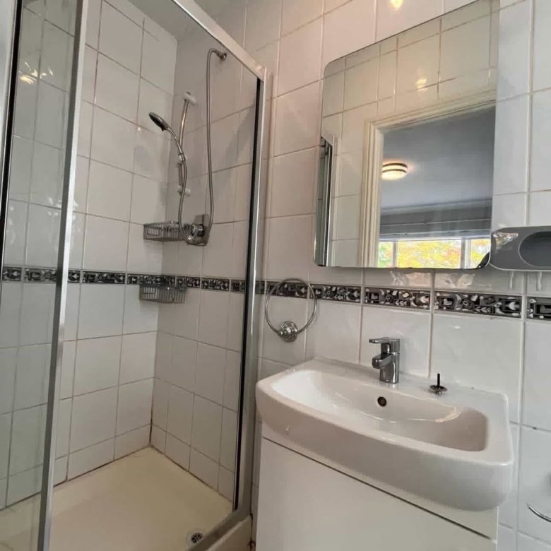 Small bathroom with shower, sink, and mirror. White tiles with decorative border.