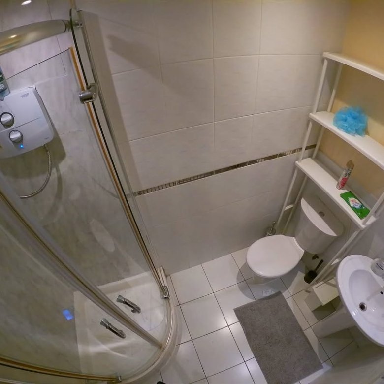 Compact bathroom with shower, toilet, sink, and storage shelf.