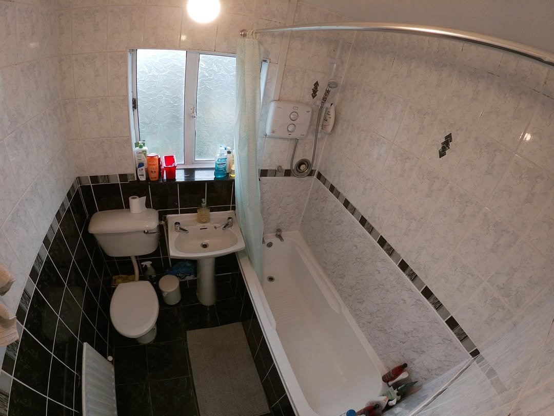 Small bathroom with toilet, sink, bathtub, shower curtain, and tiled walls.