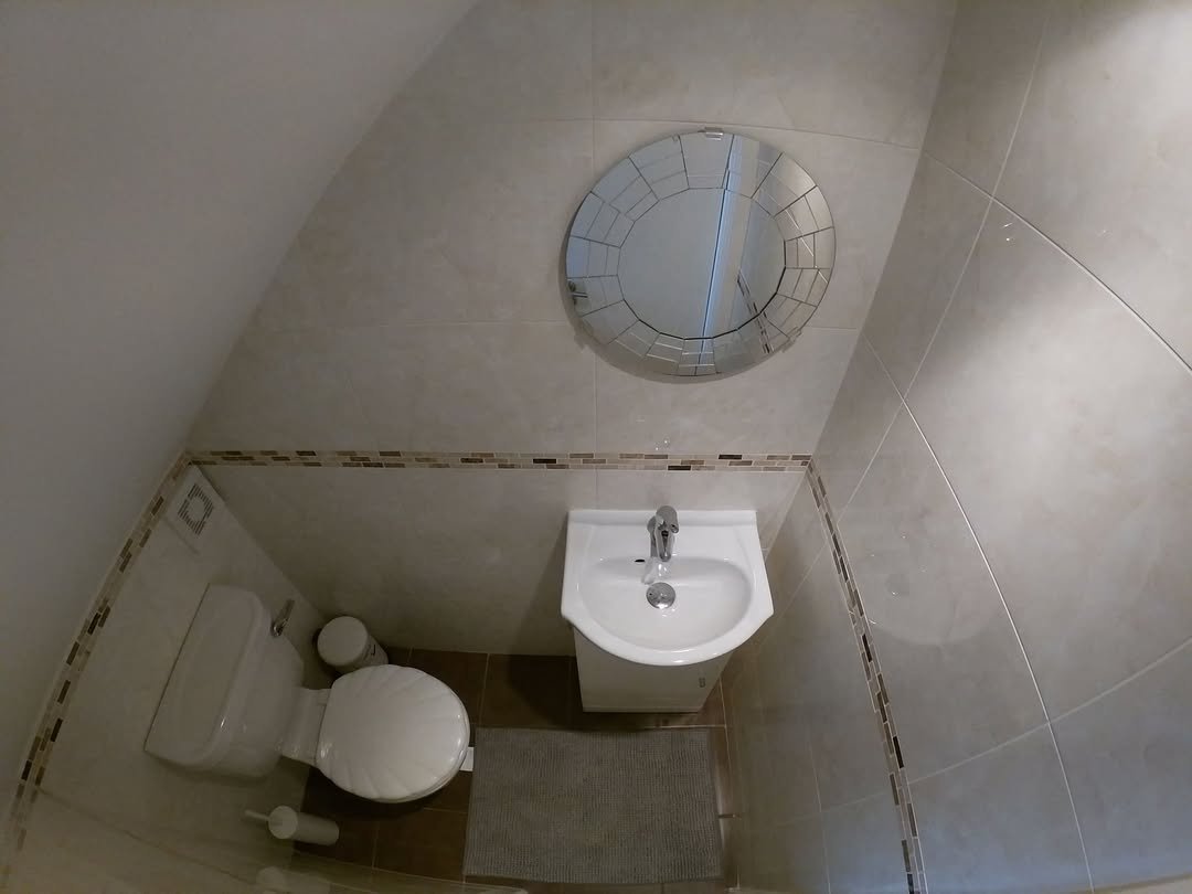 Small bathroom with toilet, sink, and round mirror under a sloped ceiling.