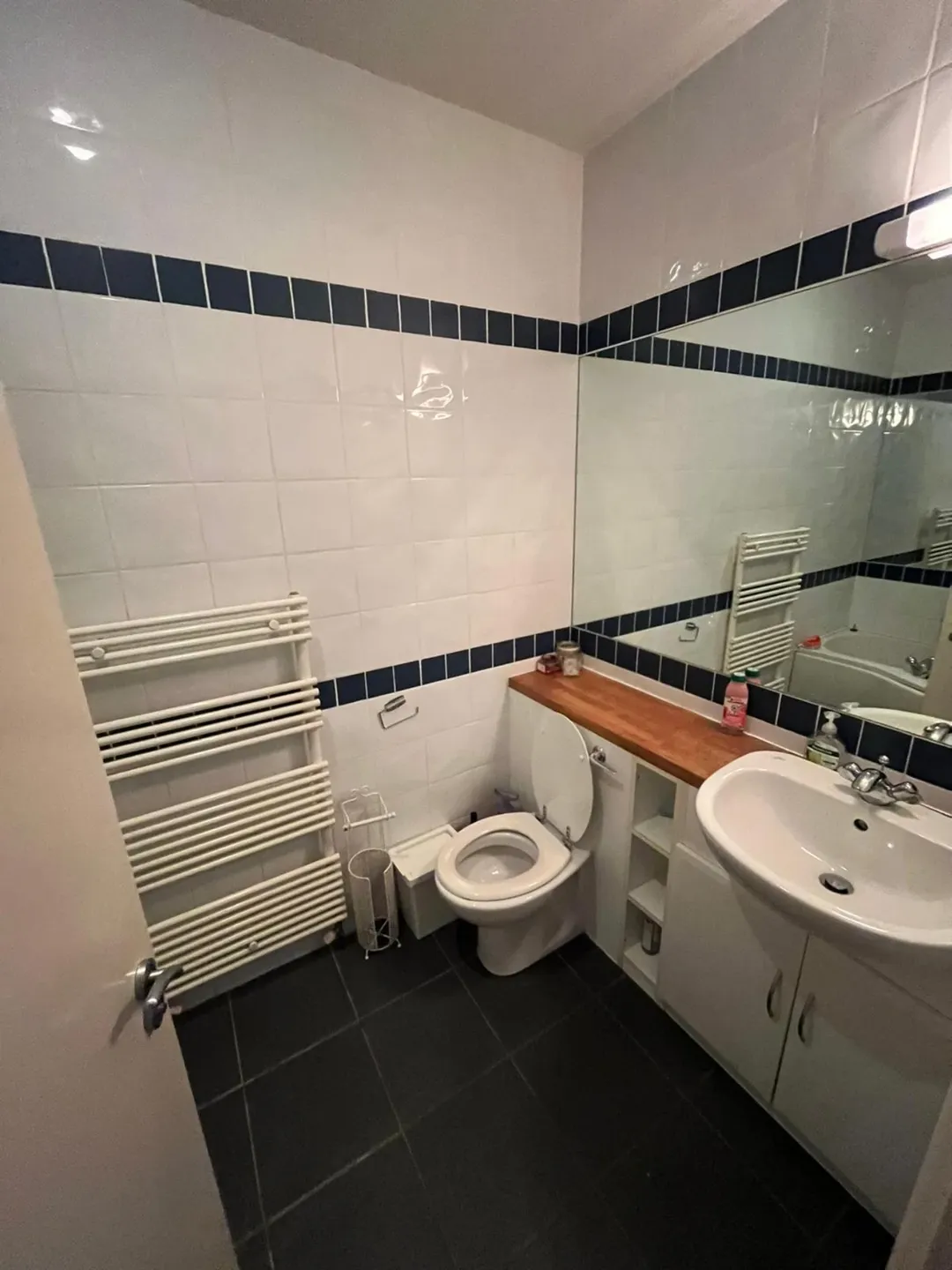 Small Bathroom White Tiles Blue Trim Small bathroom with white tiles, dark blue trim, toilet, sink, and towel rack.