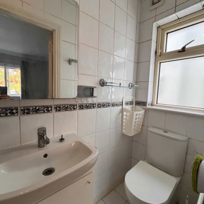 Small bathroom with white tiles, sink, toilet, and window.